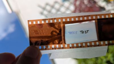 A section of photo negative with one of the image frames cut out and replaced with tape. The word test has been written twice on the tape.